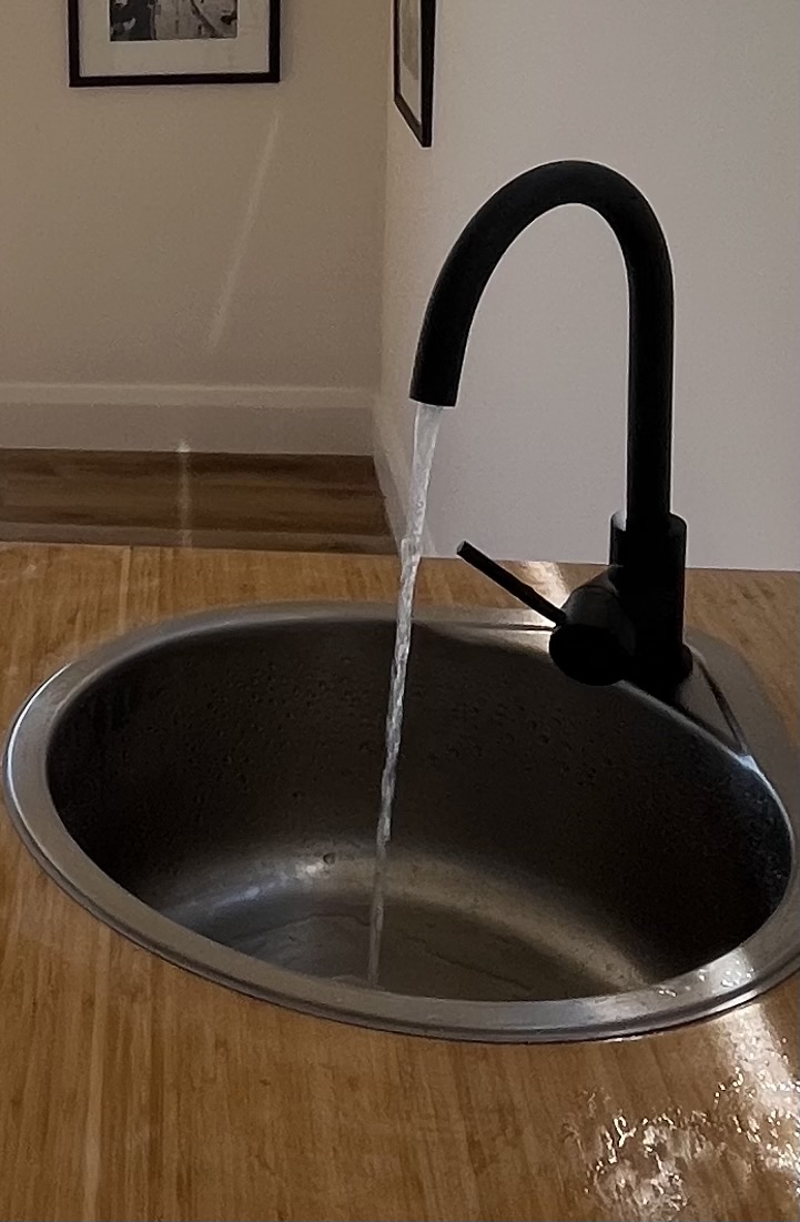 Black mixer tap running into a stainless sink